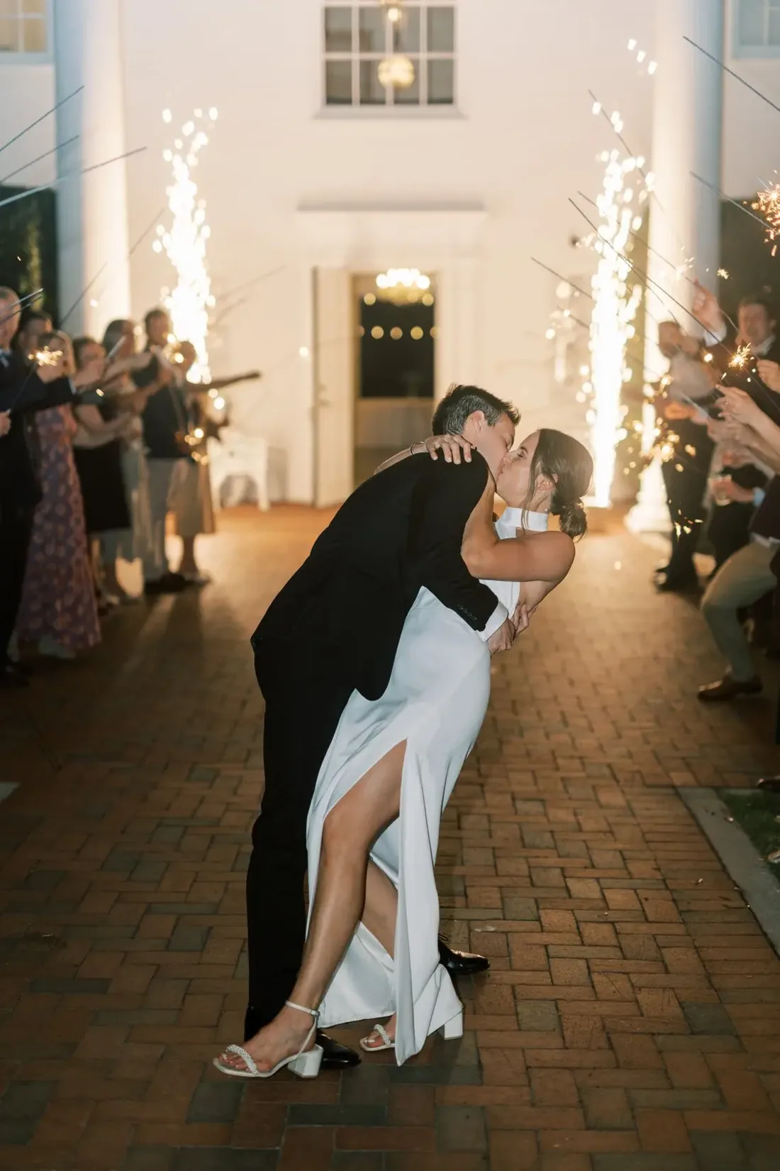 Couple sharing a dip kiss framed by cold spark fountains at a wedding send-off