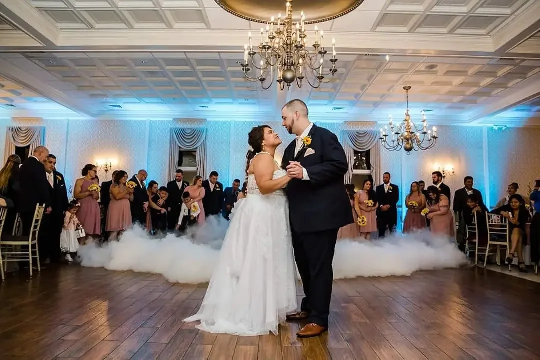 Bride and groom sharing a first dance on the clouds under blue uplighting in an elegant ballroom