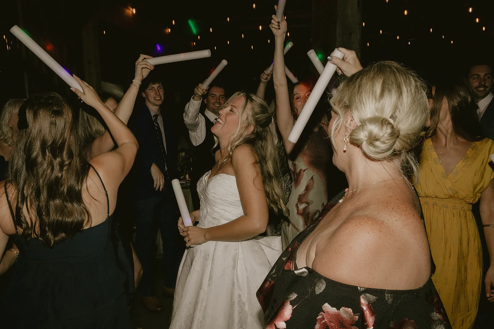 Bride dancing in the middle of a packed reception crowd waving glow sticks in the air
