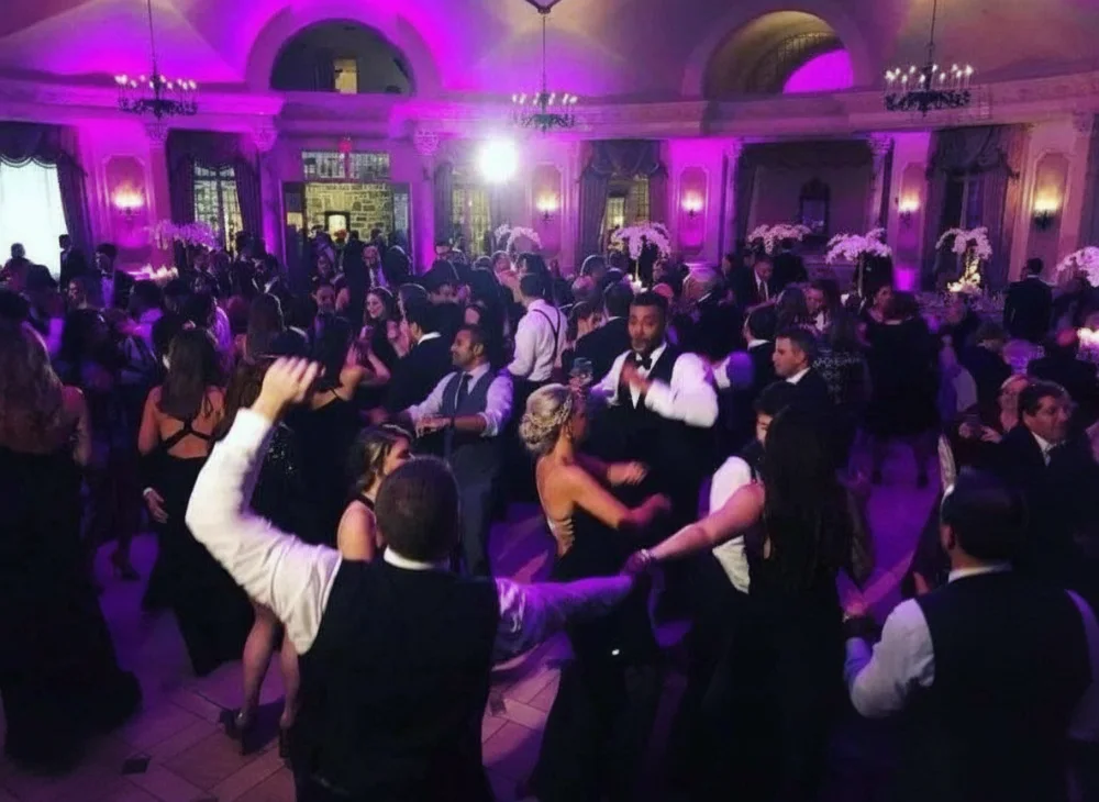 Packed wedding dance floor glowing with purple uplighting in an elegant ballroom