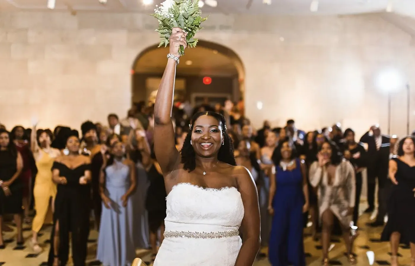 Bride celebrating with a raised bouquet on a packed dance floor